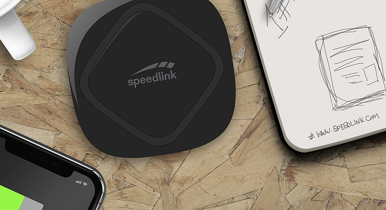 Schwarzes Speedlink Wireless-Ladegerät liegt auf einem Holztisch, daneben ein Smartphone und ein Notizblock
