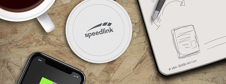 Kabelloses Ladegerät von Speedlink auf einem Holztisch, daneben ein Smartphone, eine Tasse Kaffee und ein Notizblock mit Stift