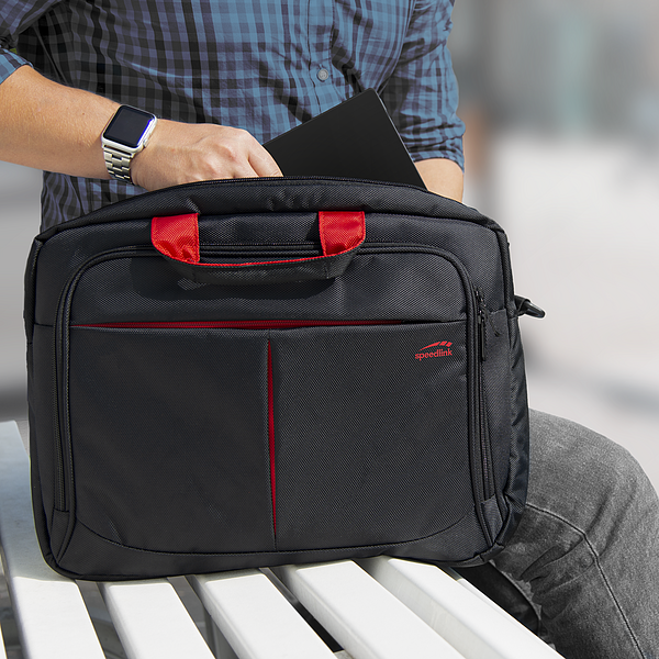 Person mit kariertem Hemd steckt ein Tablet in eine schwarze Laptoptasche mit roten Griffen auf einer Bank