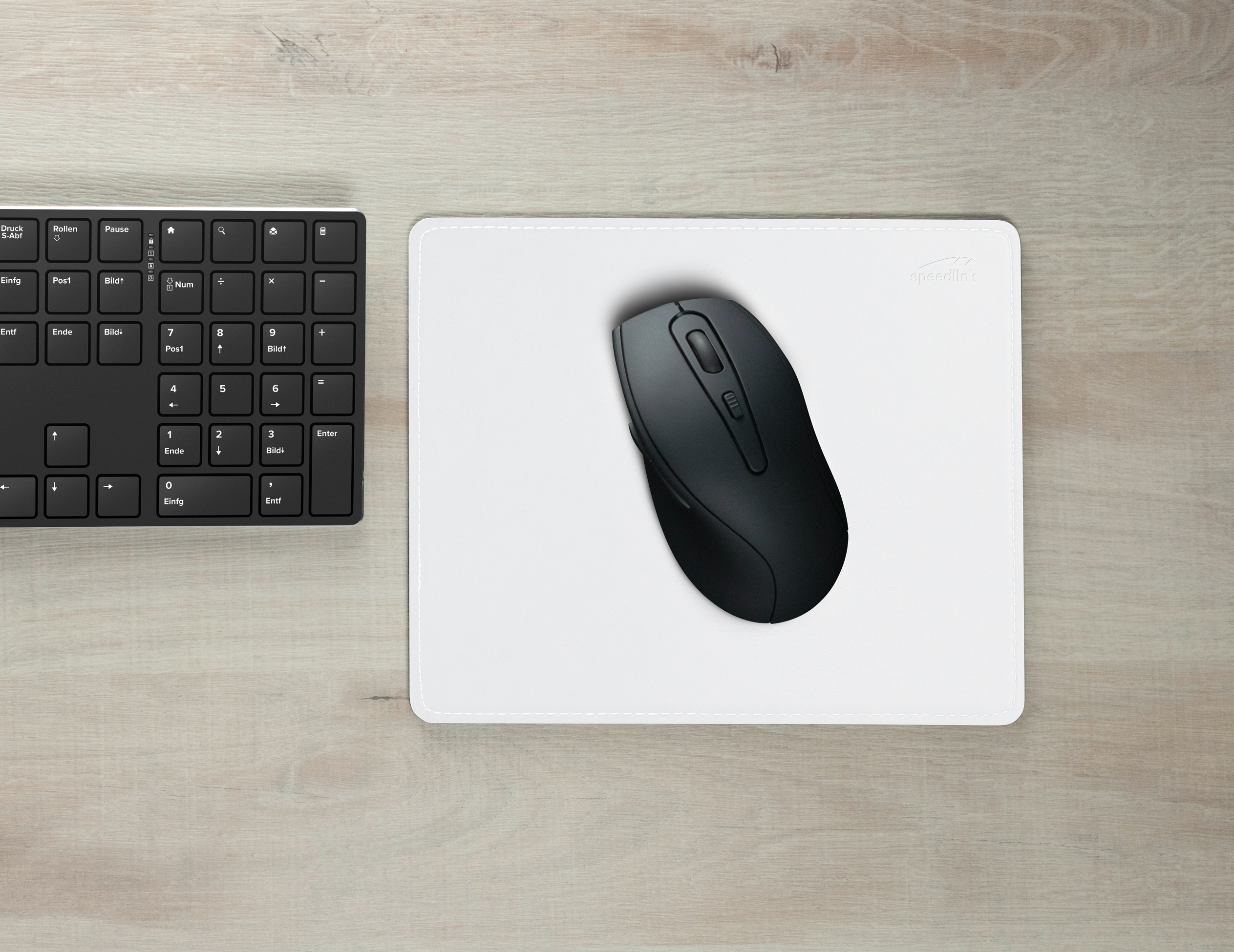 Schwarze Computermaus auf weißem Mauspad neben einer schwarzen Tastatur auf hellem Holztisch