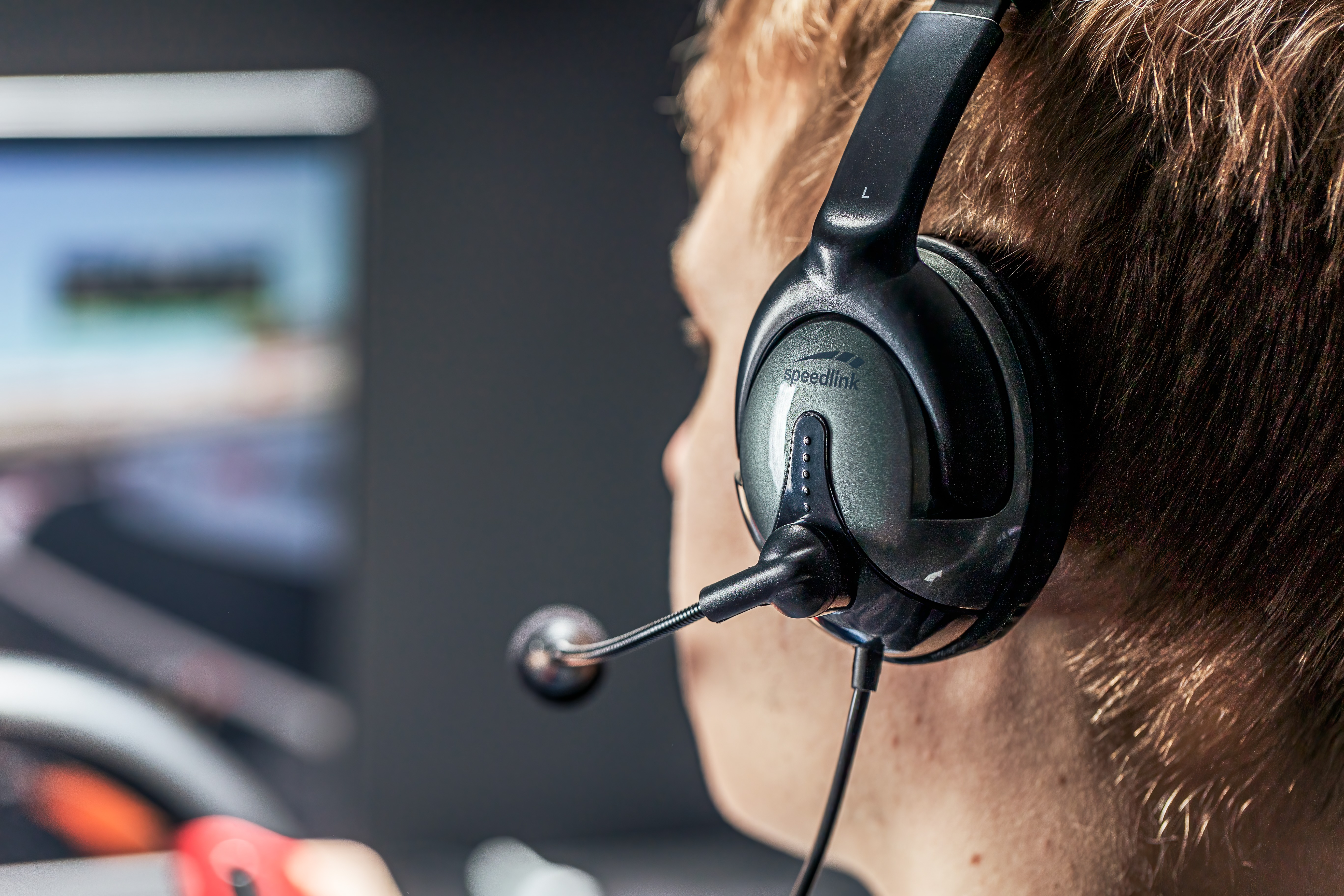 Nahaufnahme eines Gamers mit Speedlink-Headset und Mikrofon vor einem Bildschirm