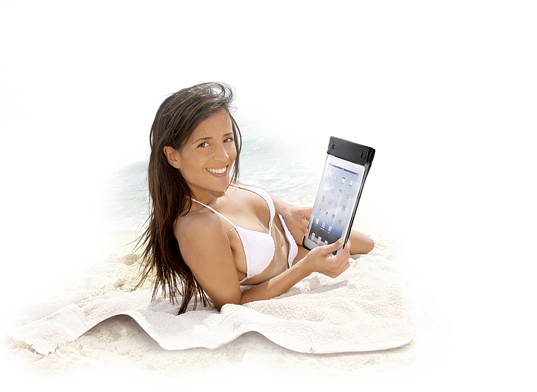 Lächelnde Frau im weißen Bikini liegt am Strand auf einem Handtuch und hält ein Tablet in einer wasserdichten Schutzhülle