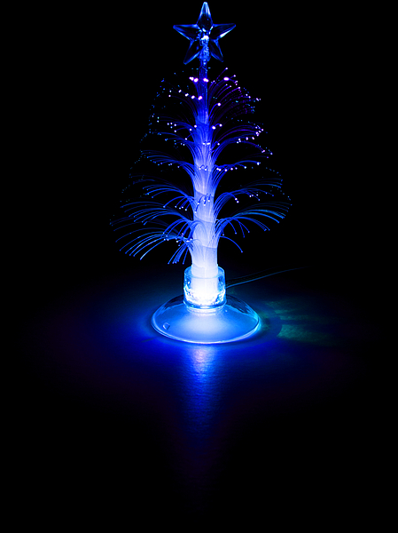 Kleiner, leuchtender LED-Weihnachtsbaum aus Fasern mit blauem Licht und Stern auf dunklem Hintergrund
