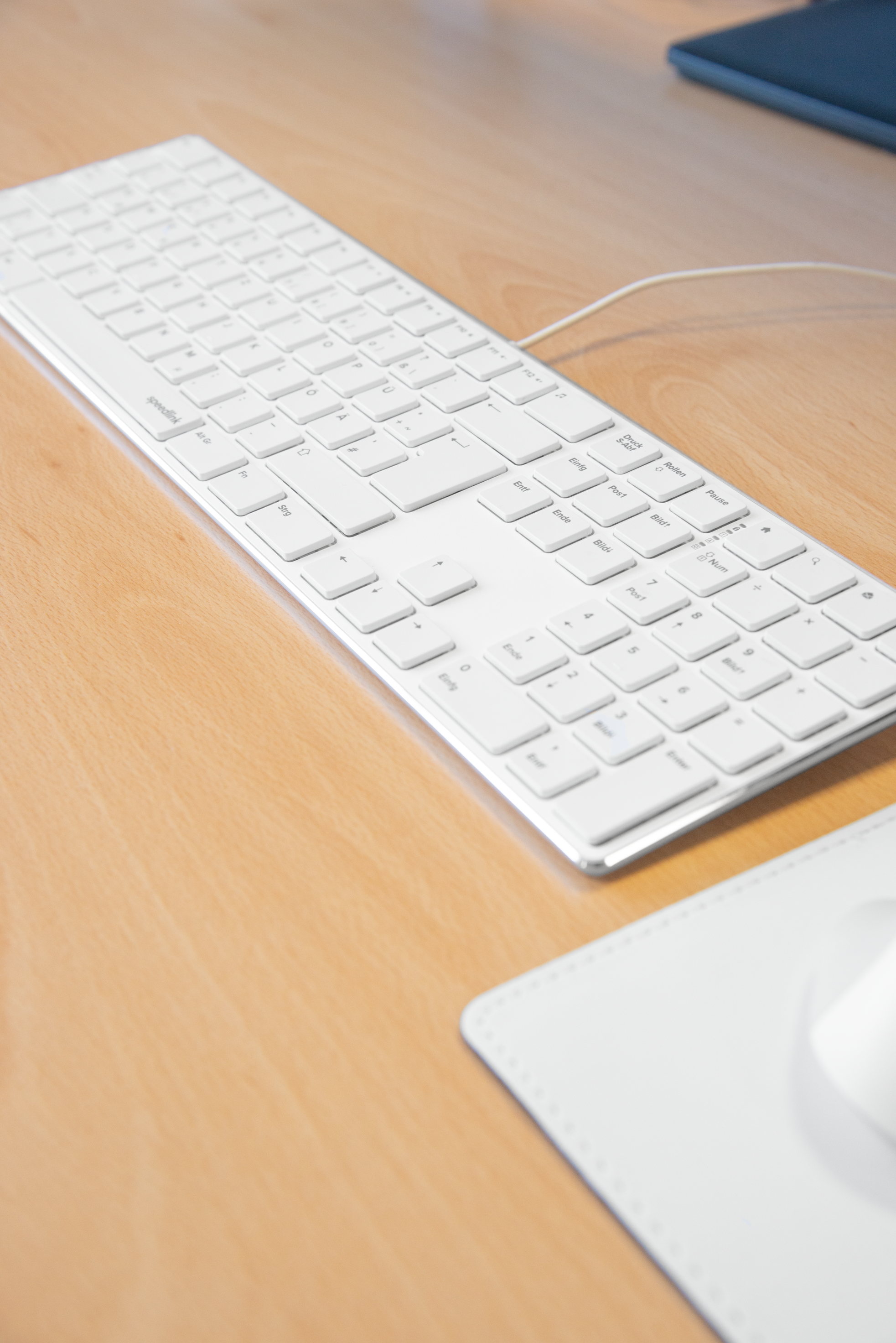 Weiße flache Tastatur mit Zahlenblock auf hellem Holztisch neben weißem Mauspad