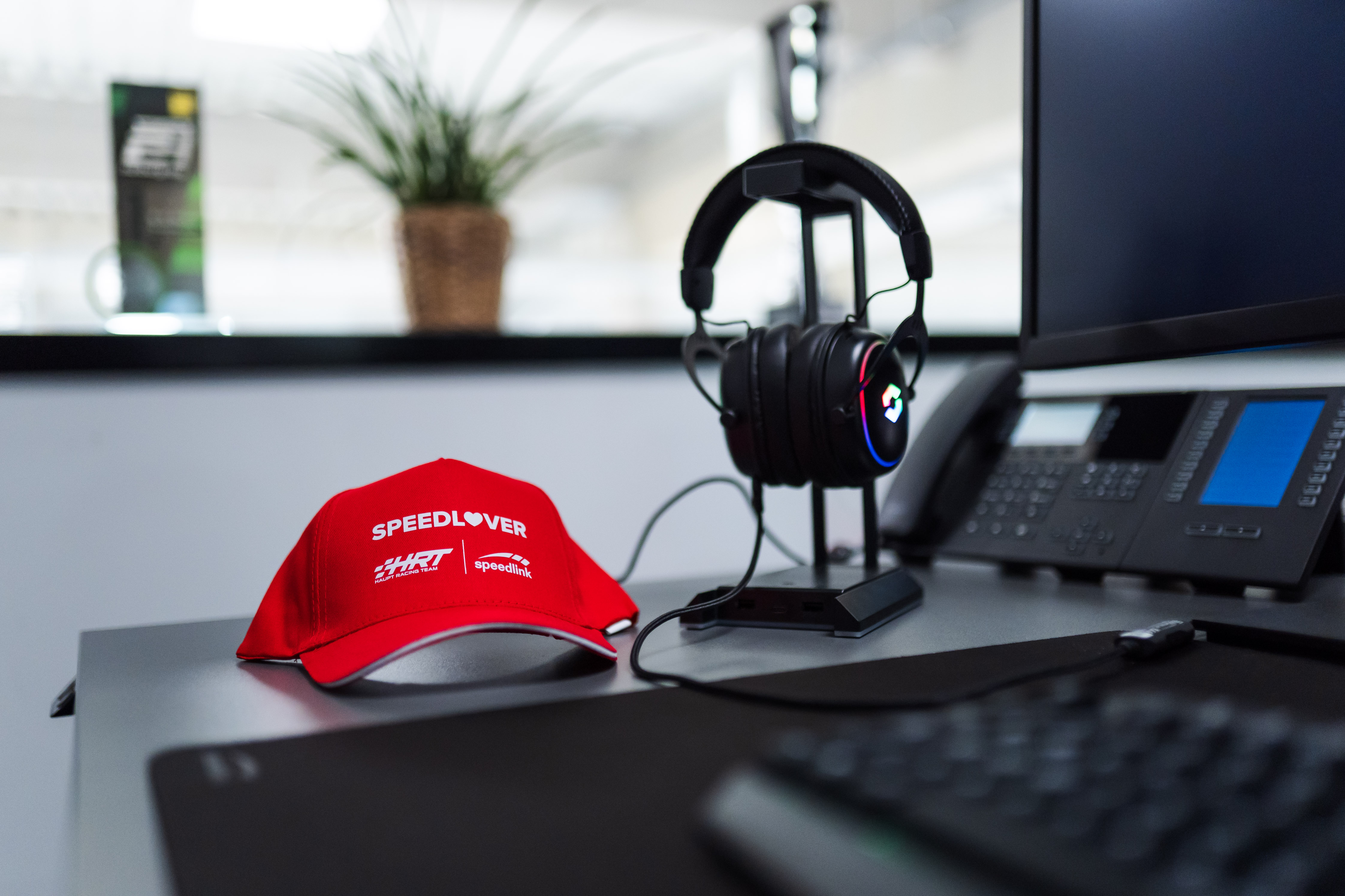 Rote SPEEDLOVER-Basecap, Gaming-Headset mit LED-Beleuchtung und Büro-Equipment auf einem Schreibtisch