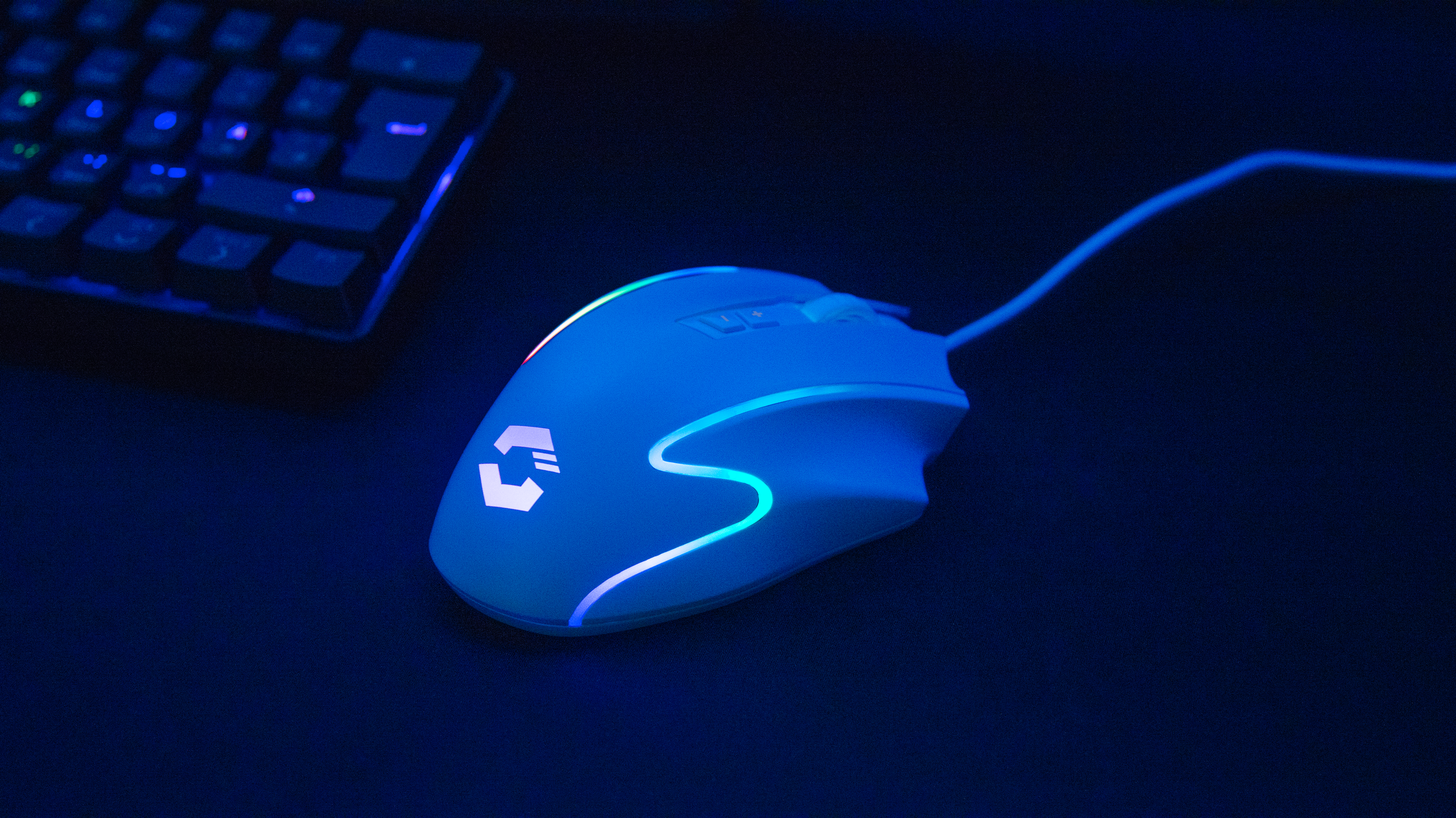 Weiße Gaming-Maus mit LED-Beleuchtung und Kabel neben einer Tastatur auf dunklem Untergrund