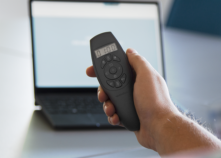 Hand hält eine schwarze Präsentationsfernbedienung mit Display vor einem unscharfen Laptop-Bildschirm