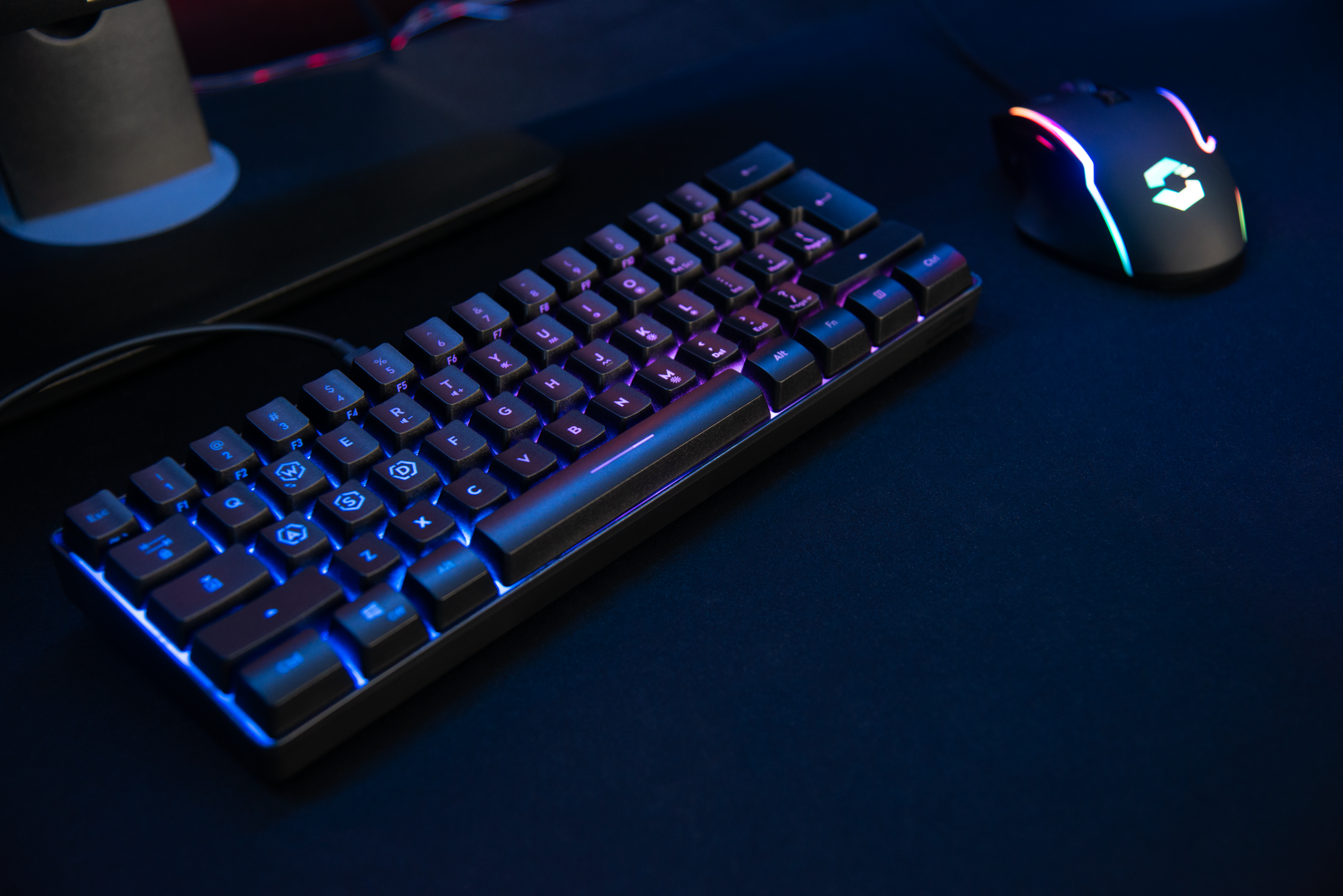Mechanische Gaming-Tastatur mit blauer und violetter RGB-Beleuchtung neben einer beleuchteten Gaming-Maus auf einem dunklen Schreibtisch