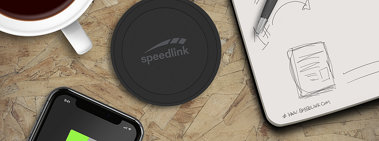 Rundes Speedlink Wireless Charger Ladepad neben Smartphone mit Ladeanzeige, Tasse Kaffee und Notizblock auf Holzoberfläche
