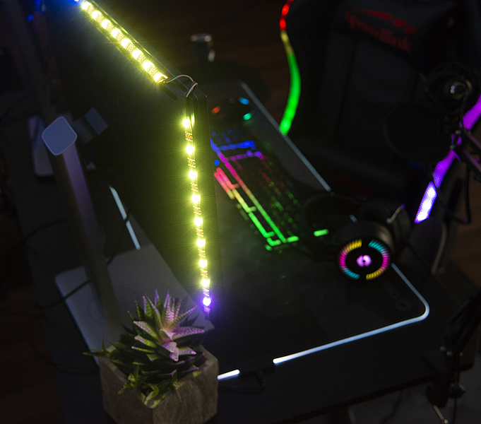 Schreibtisch mit LED-beleuchtetem Monitor, RGB-Tastatur, Gaming-Stuhl, Headset und einer kleinen Pflanze