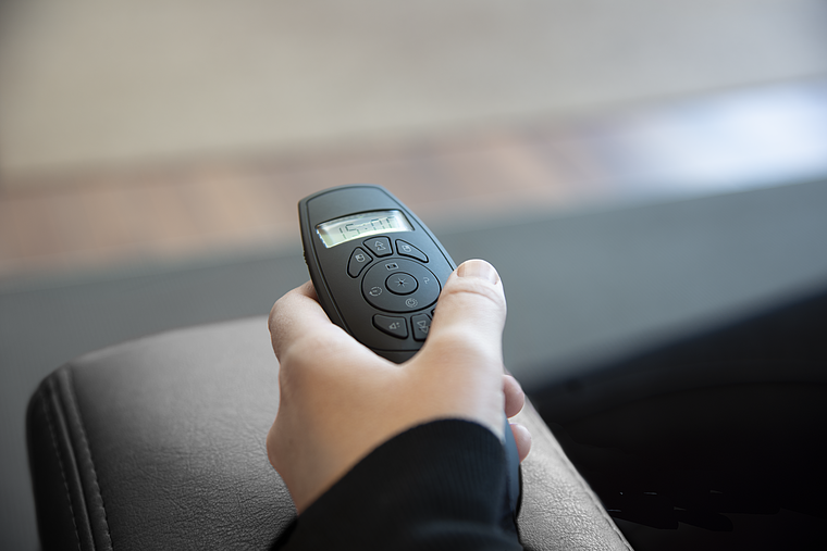 Nahaufnahme einer Hand, die eine Fernbedienung mit Display und mehreren Tasten für einen elektrischen Sessel bedient